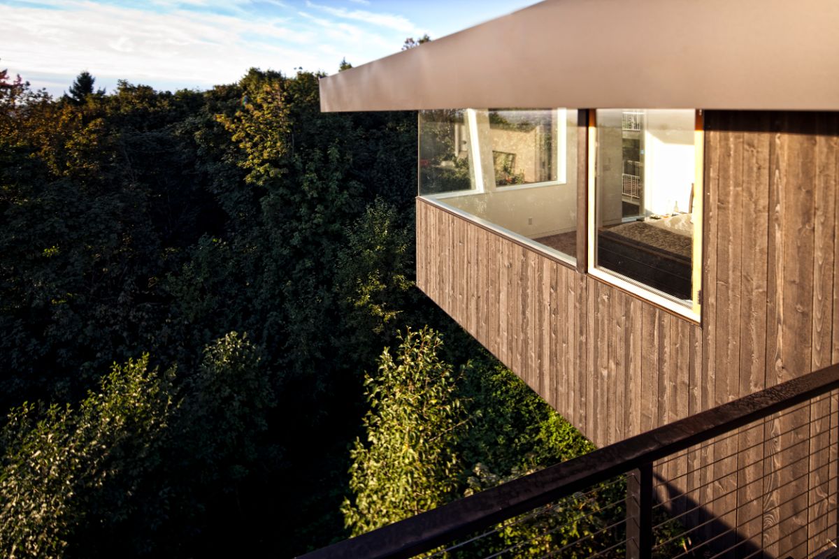 The bedroom features large glass windows that showcase the view of the surrounding trees.