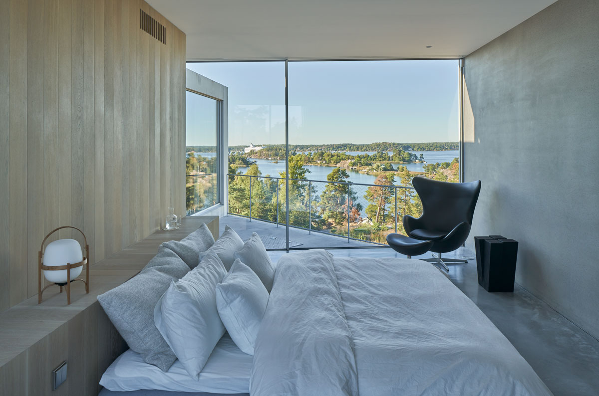 The bedroom features a full-size glass wall that showcases the view of the beach.