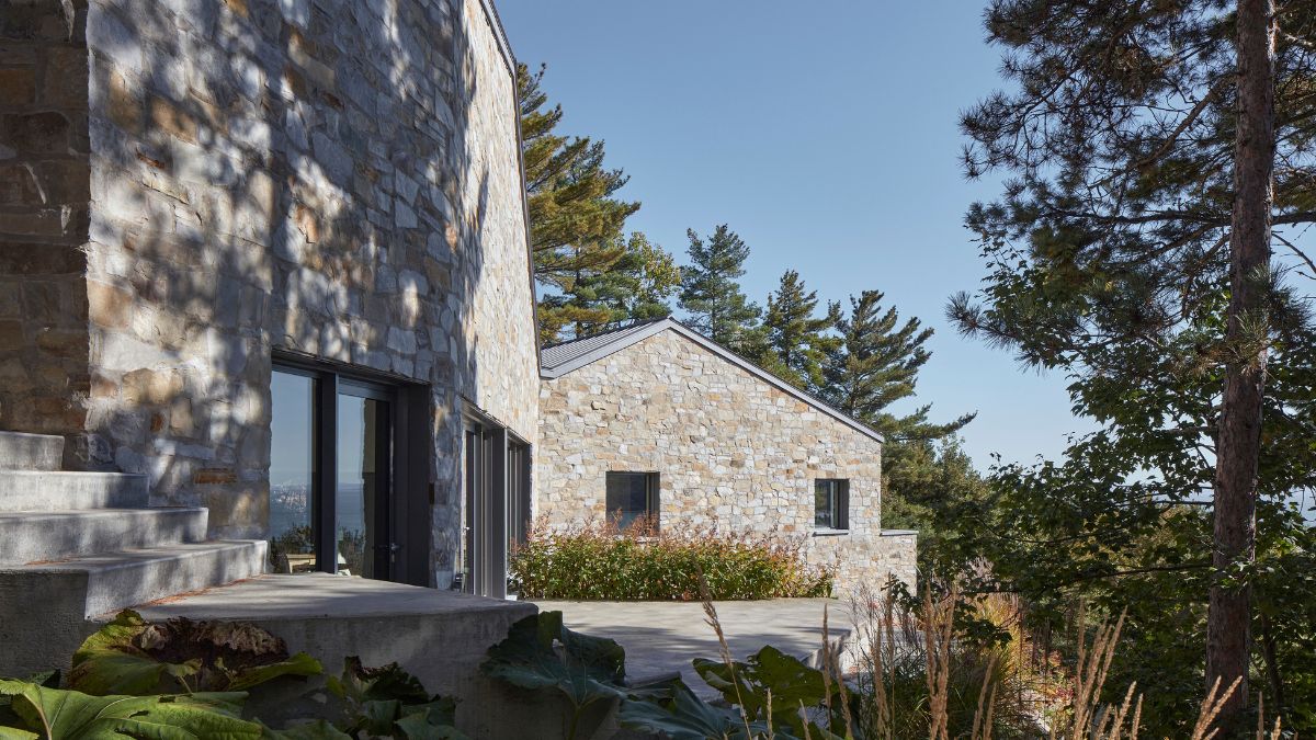 The image depicts a stone house captured from an exterior perspective, featuring lush vegetation enveloping the premises.