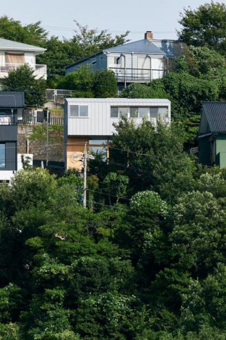 The scene depicts a residence situated atop a verdant hillside, captured from an aerial perspective.