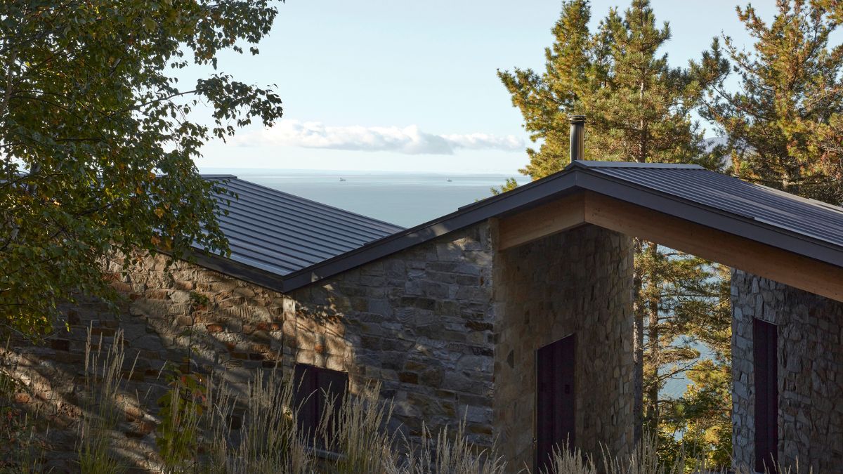 A structure constructed of stone and topped with a metal roof is situated adjacent to a cluster of trees.