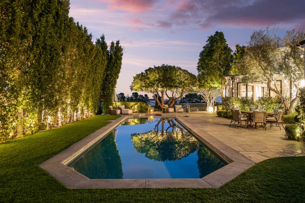 The saltwater pool is surrounded by beautiful grass and tall hedge plants.