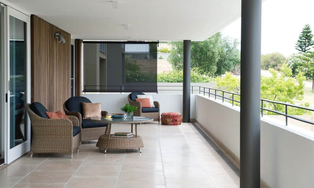 Covered balcony with cushioned wicker seats, a matching coffee table, round columns, and sweeping views of the lush yard.