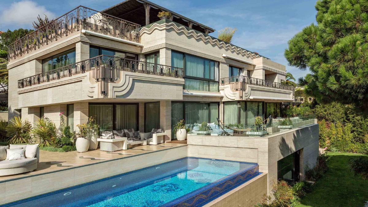 This daytime exterior shot features different sections of the house, including a small pool, as well as the unique design elements such as the wavy patterns on the walls and intricate stone carvings.