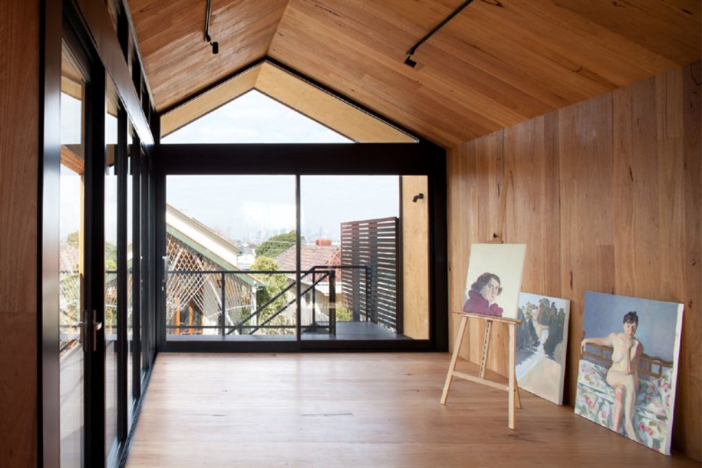 An interior shot of a room showcasing the floors, walls and ceiling that are made of blackbutt and plywood, while also featuring some of the owner's paintings or artworks.