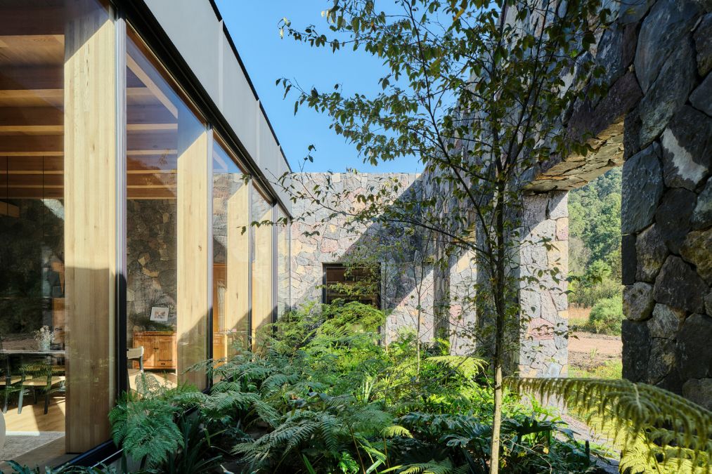 The FS House is adorned with a stone wall, with trees situated in front of the property.