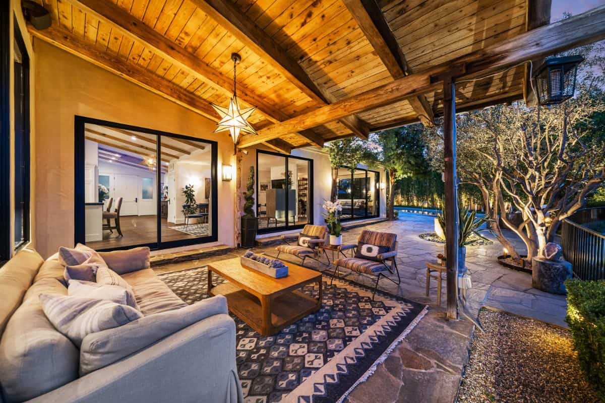 The covered porch is furnished with a gray sofa, striped armchairs, and a wooden coffee table over a vintage area rug.