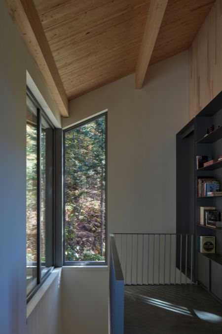 A photograph capturing the interior of the upper level of a house, revealing a prominent bookshelf and expansive windows.