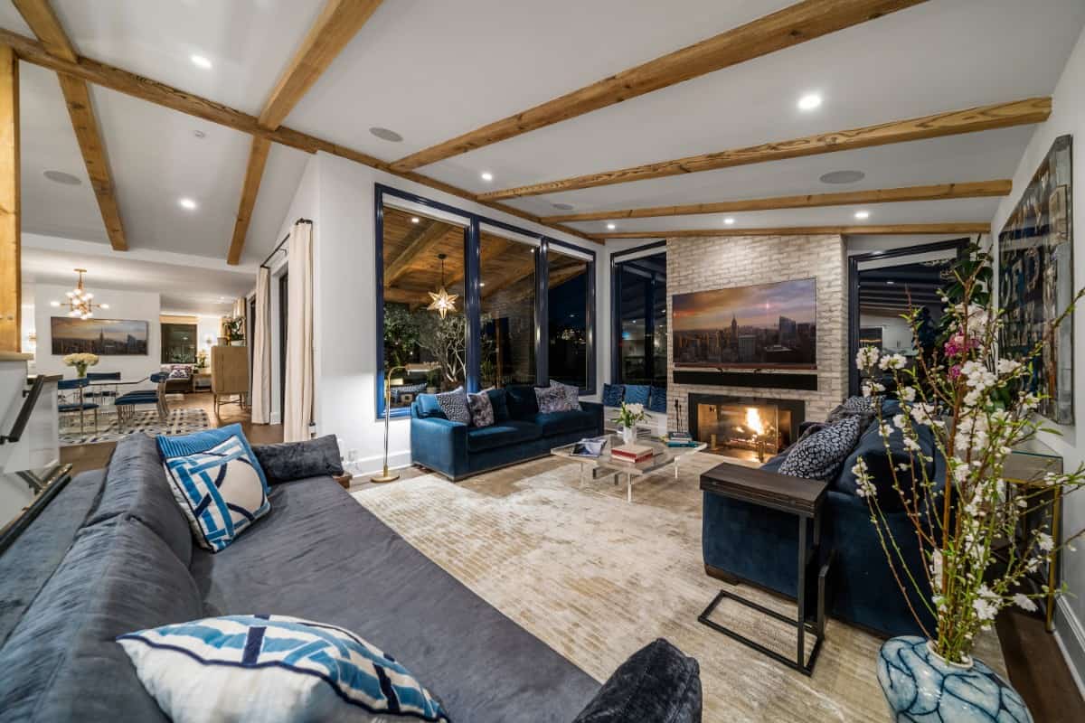 The recessed living room has velvet sofas, a beamed ceiling, and a brick fireplace.