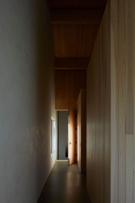 A prolonged hallway is presented, culminating in an open door of a specific room and illuminated by natural light emanating from a nearby window.