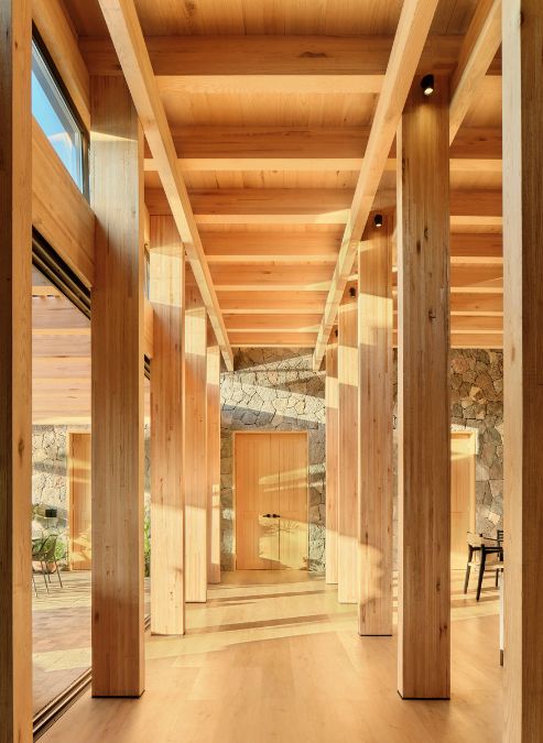 The lengthy hallway is adorned with wooden columns and features a stone wall.