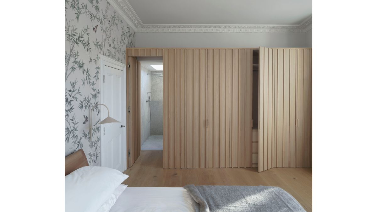 White sheets and a lovely wallpaper cover the bed in the bedroom, which has a color scheme of white and grey.