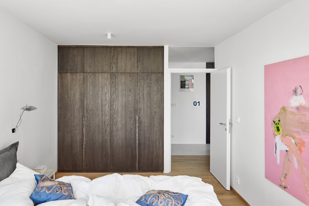 This is an interior shot of a spacious bedroom, featuring full-height brown cabinets and a pink wall art gallery mounted above the bed.