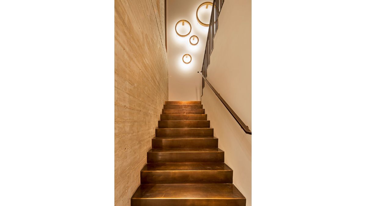 Because of the chandelier that provides light, the staircase has a blend of white, brown, and beige.