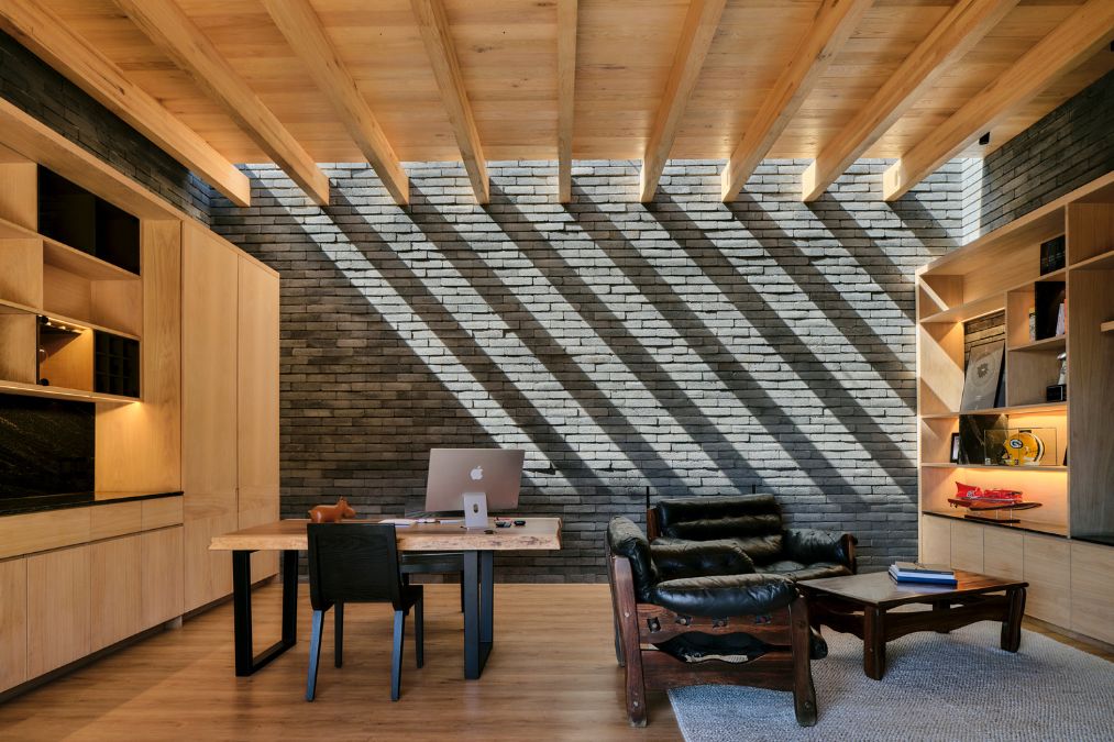 The spacious office area of the house features a gray brick-tiled wall and exposed wooden beams.