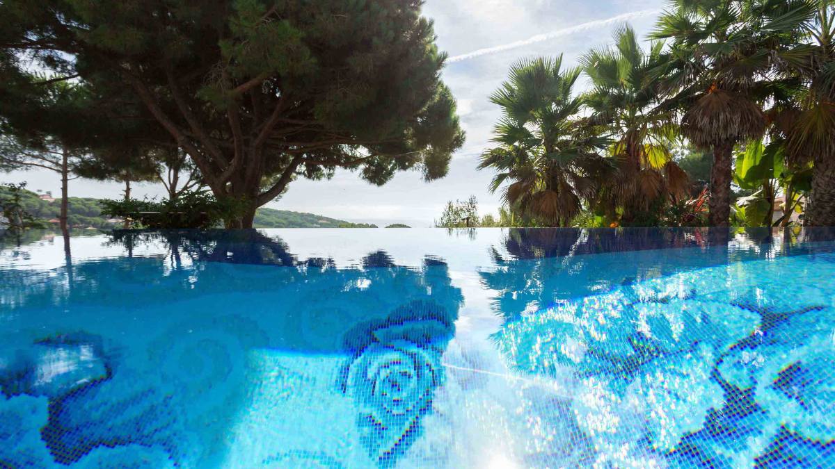 An infinity pool is situated outdoors, surrounded by abundant trees.