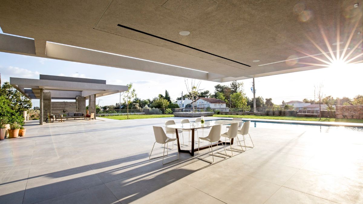 A dining table is situated outside with a view of the house's greenery and pool.