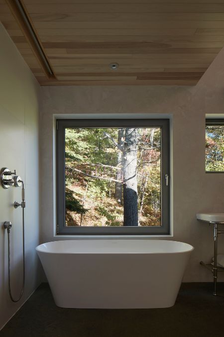 A bathroom is showcased, featuring a bathtub and a sizable window that offers an outside surroundings view.