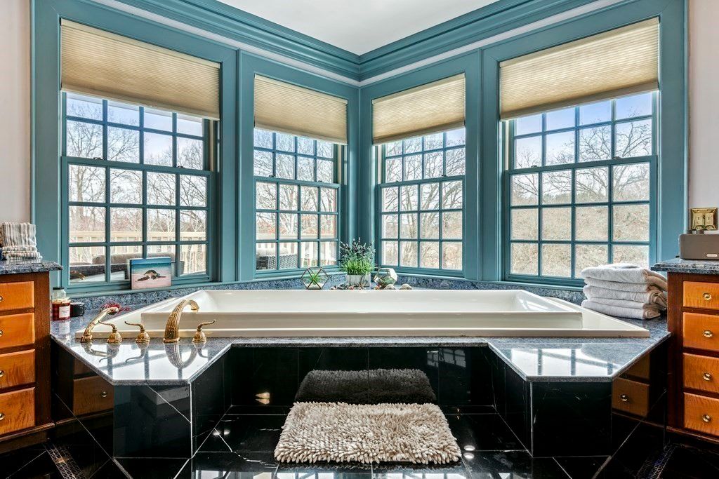 The bathroom features a built-in tub by the glass windows that showcases the view of the river, and the gold-plated fixtures give off a luxurious feel.