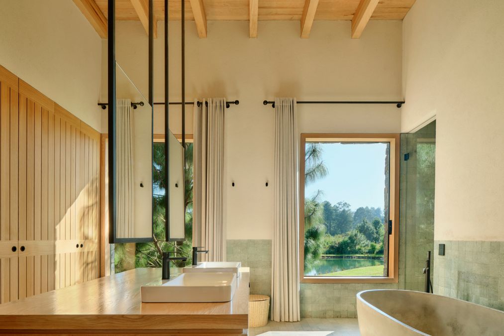 The bathroom is equipped with a bathtub and a window that provides views of green surroundings, complemented by minimalist wooden accents.