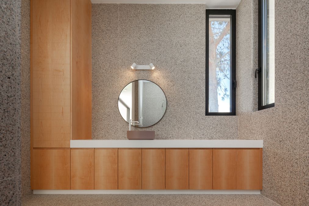 This is a photograph focusing on a specific section of the bathroom, highlighting a single basin sink, a round mirror, and wooden cabinetry.