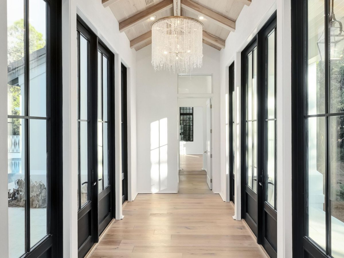 The house features a hallway with wooden flooring, glass doors, and a chandelier that illuminates the place.