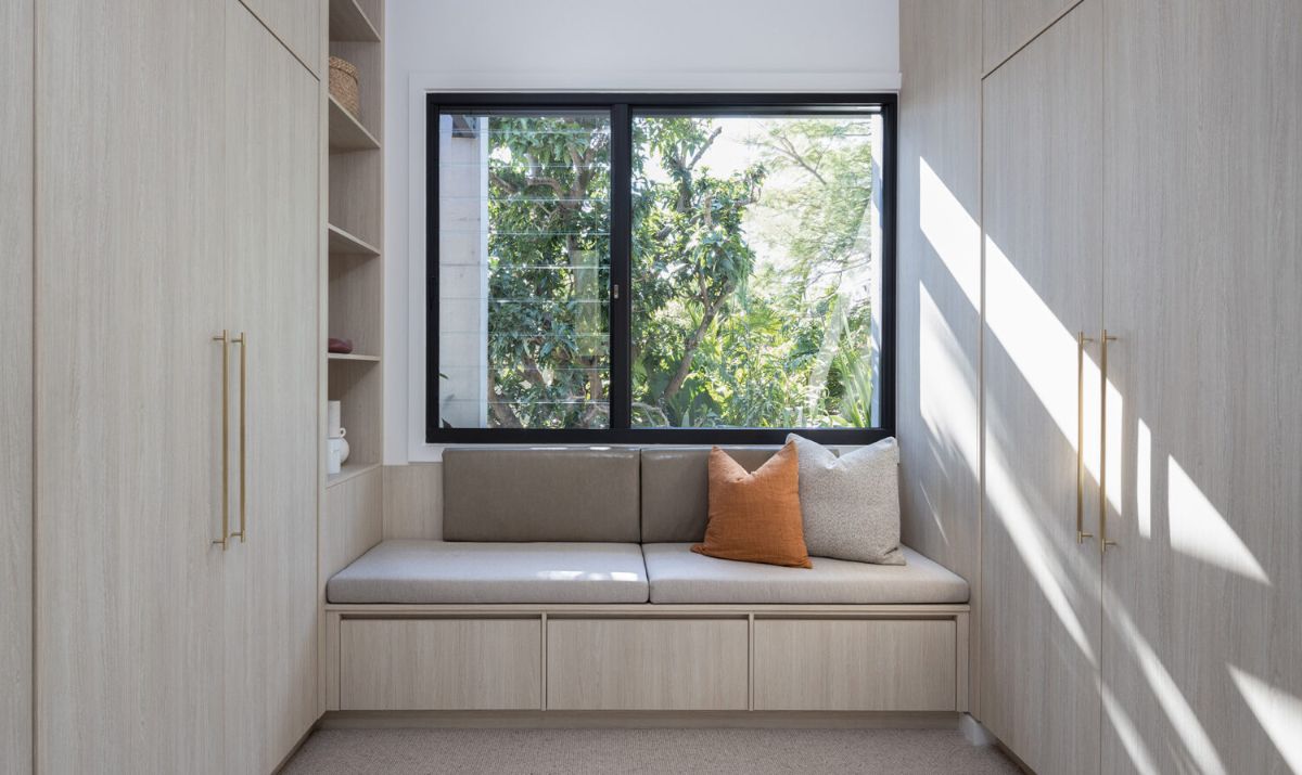 A seating area between the large wooden shelving units, with a glass window allowing sunlight to enter.