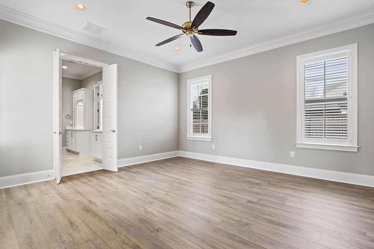 The primary bedroom has a hardwood floor, louvered windows, and a private bath enclosed in double white doors.