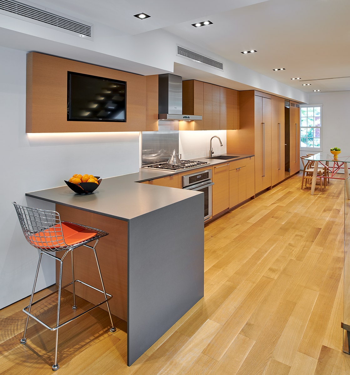 An open kitchen and dining area with light wood flooring, cabinets, and built-in appliances.