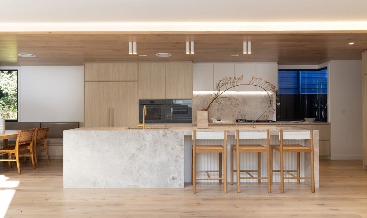 A minimalist kitchen with a long island and bar stool chairs, built-in appliances, and exposed lighting.