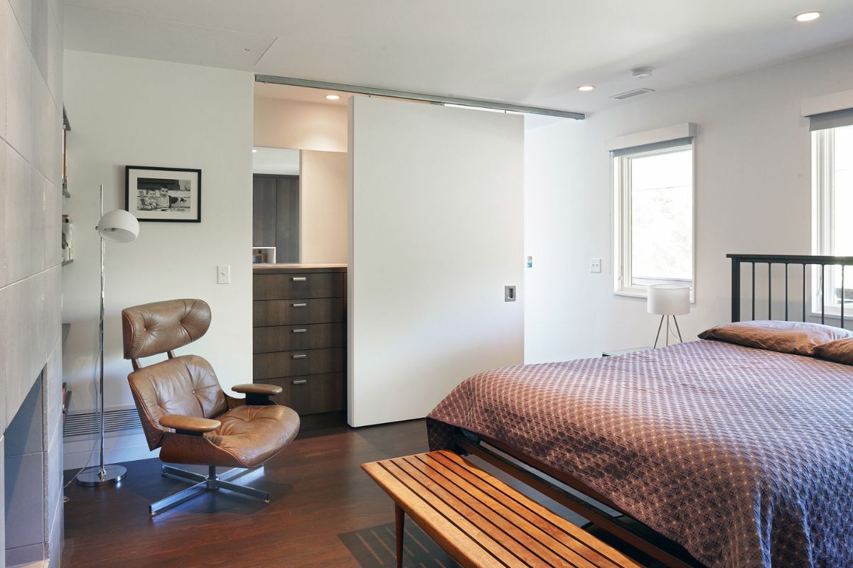 A fireplace-equipped bedroom with dark wood flooring, white walls and ceiling, and built-in millwork storage.