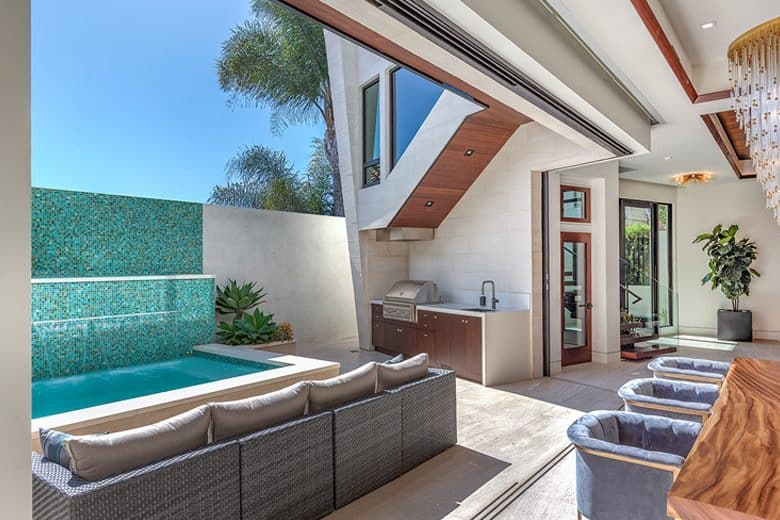 The pool terrace is surrounded by wicker seats and a built-in grill.