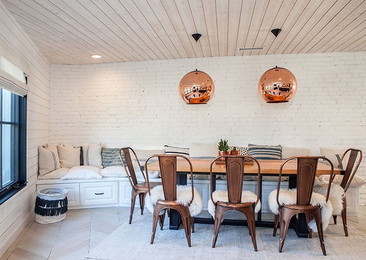 The breakfast area offers a wooden dining table paired with copper chairs and a built-in bench.