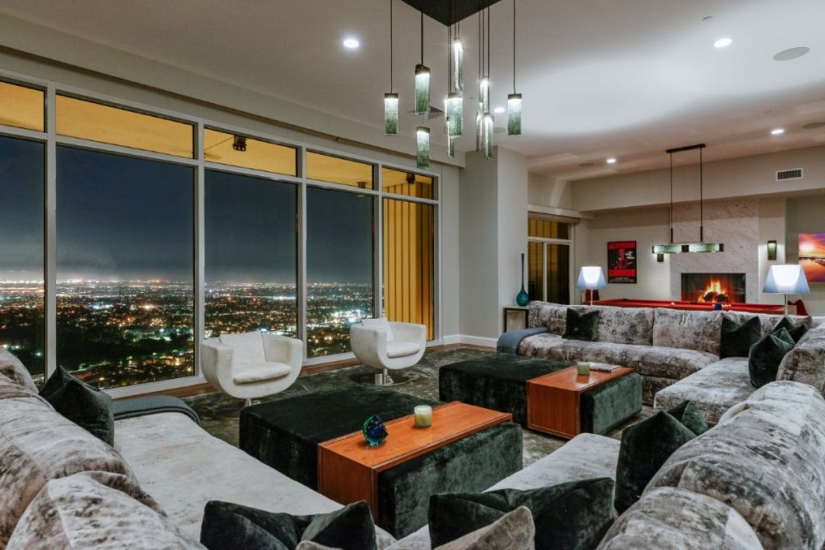 The living room features enormous sofas, floor-to-ceiling windows, and a carpeted floor.