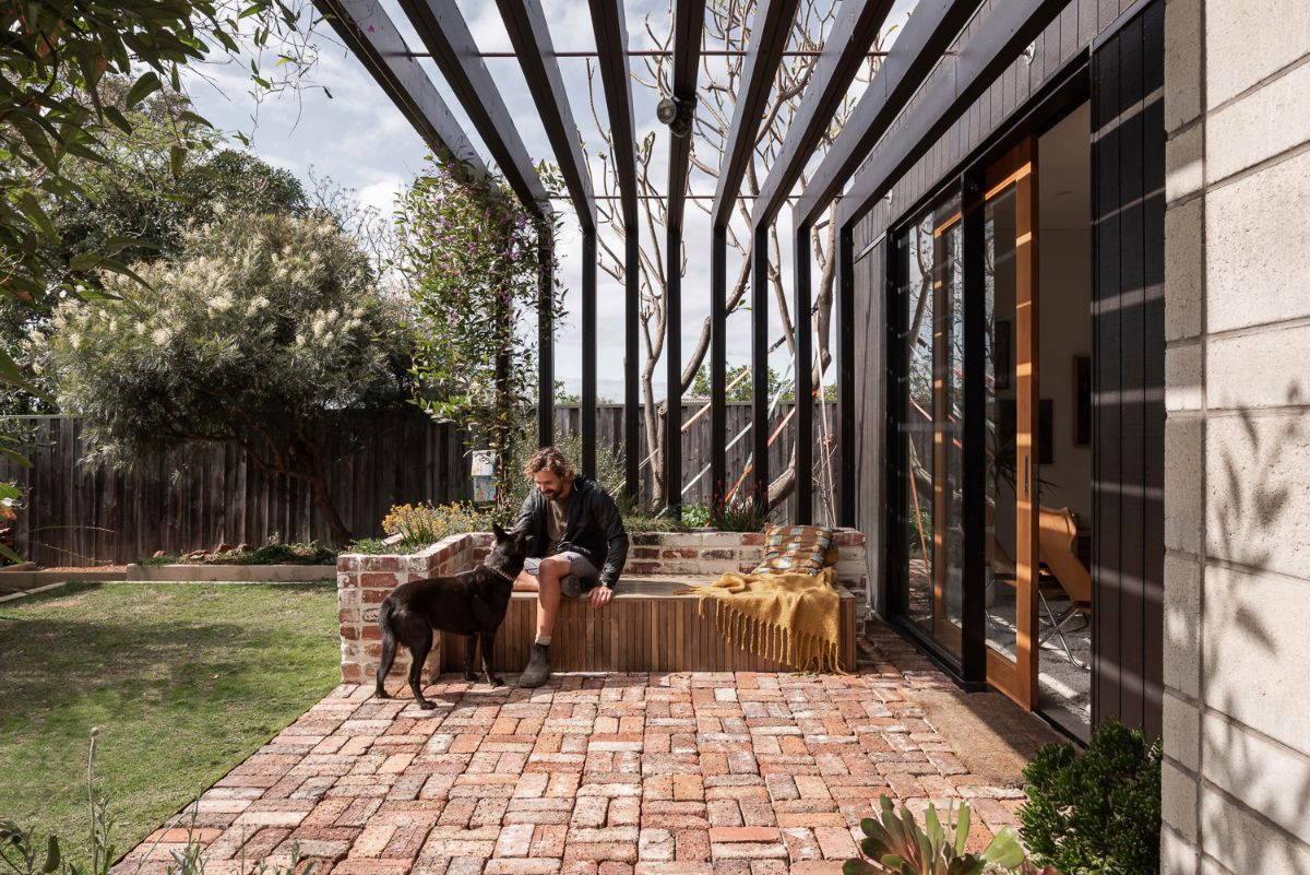 A man with a dog sits in the semi-open patio area near to the garden.