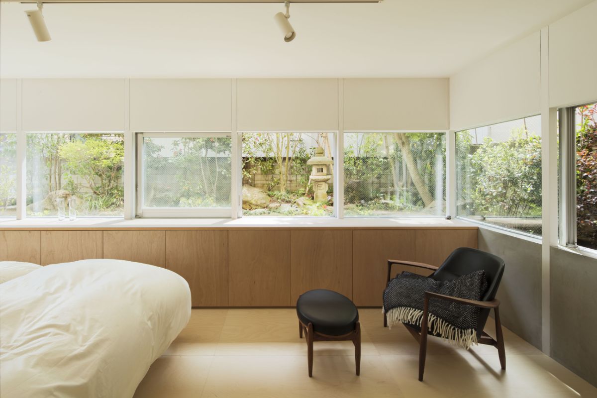 The bedroom, which has a single seating area, clean-lined cabinetry, exposed lighting, and a glass slit that provides a view of the garden.