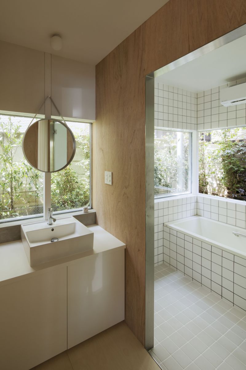 The bathroom, which includes a counter-topped sink, a round mirror suspended in a glass slit, and a built-in soaking tub.