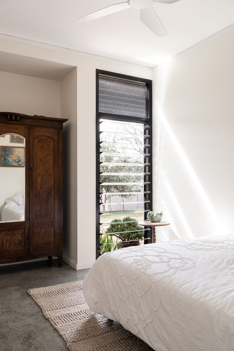 A dark wood classic dresser and a full-width jalousie window grace the master bedroom.