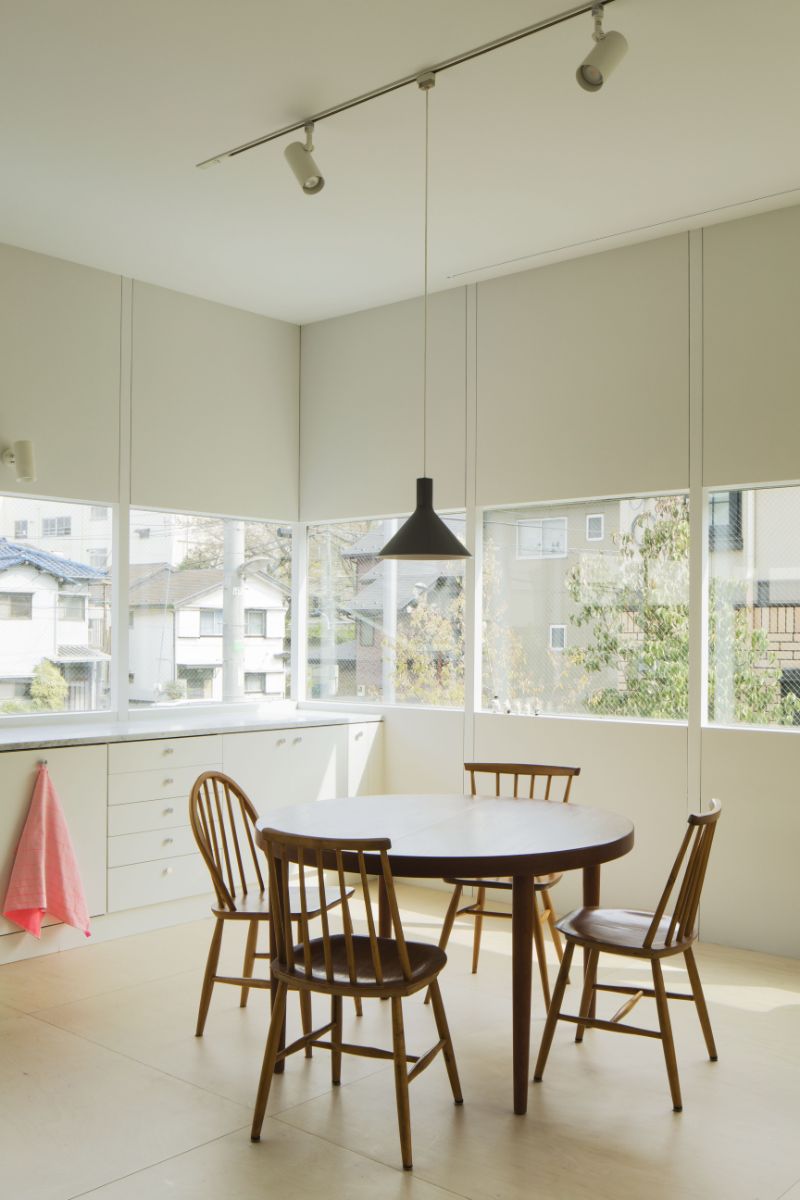 The dining room, which has a four-seater round table, pendant lighting, and a view of the neighboring houses through a glass slit.