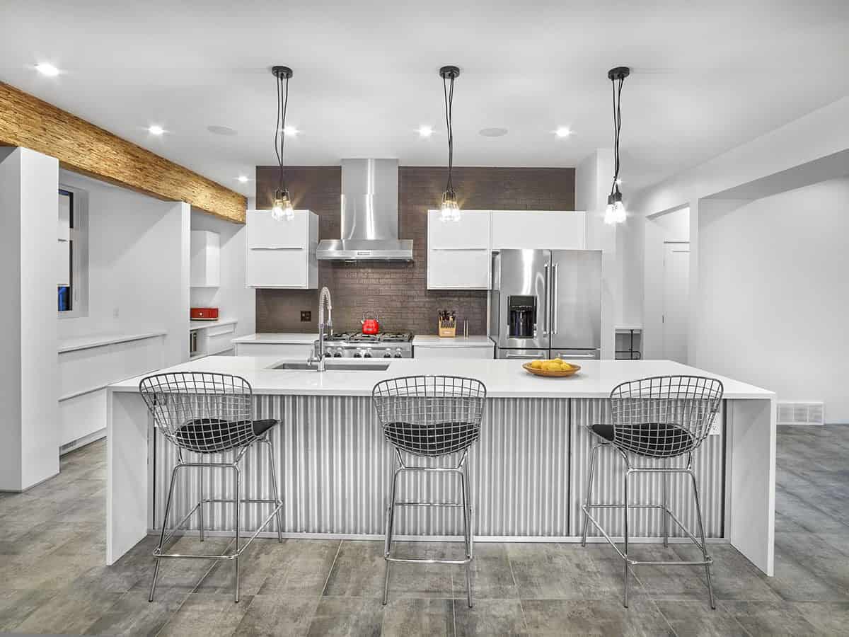 The kitchen features top-of-the-line appliances, white cabinets, and a breakfast island paired with metal bar stools.