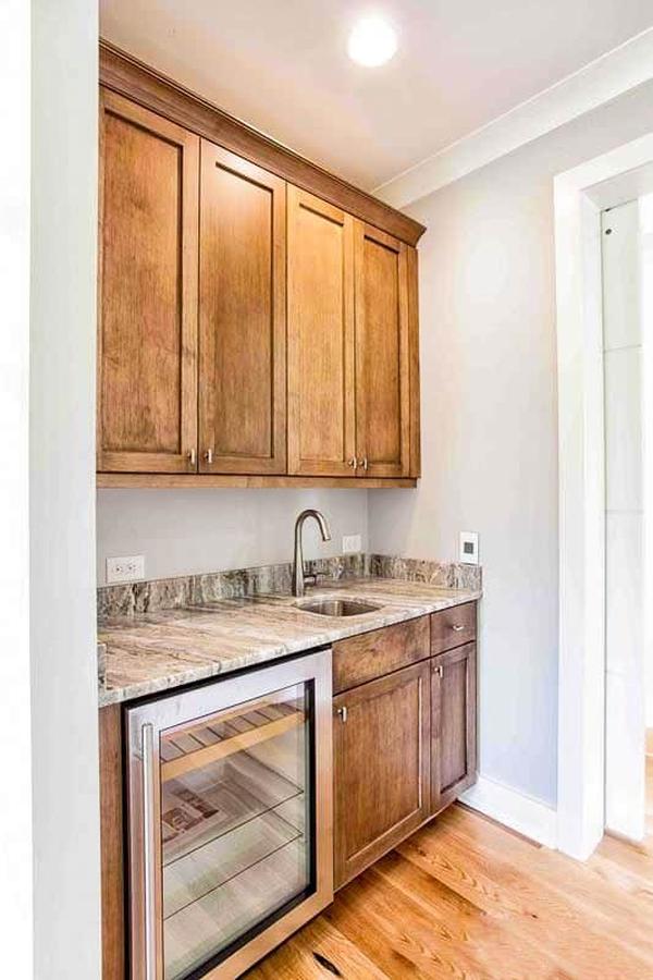 Walk-in pantry filled with wooden cabinets, a beverage fridge, and marble countertop fitted with an undermount sink.