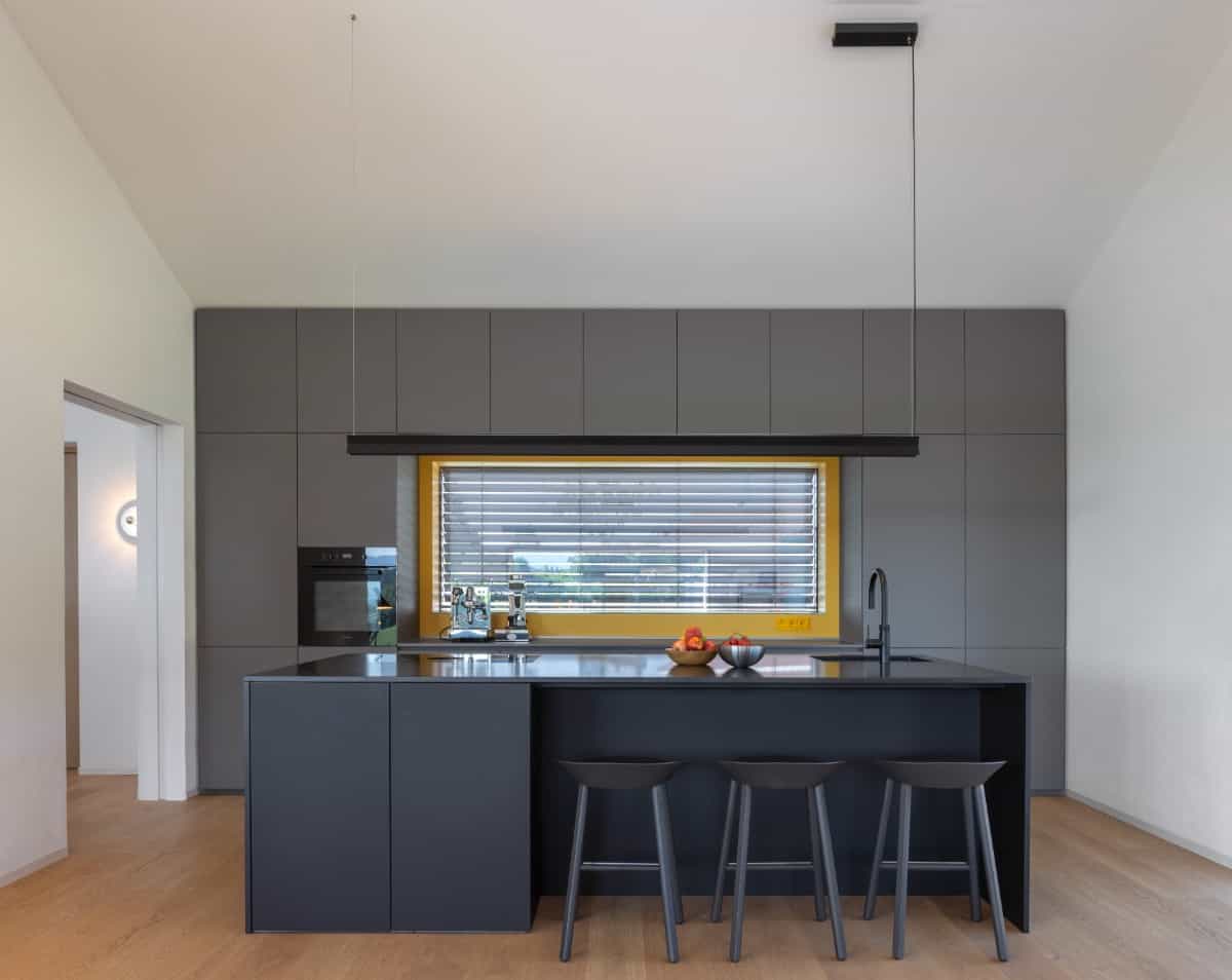 Sleek and dark cabinets, an elongated linear pendant, and a waterfall island with bar seating enhance the kitchen's modern appeal.