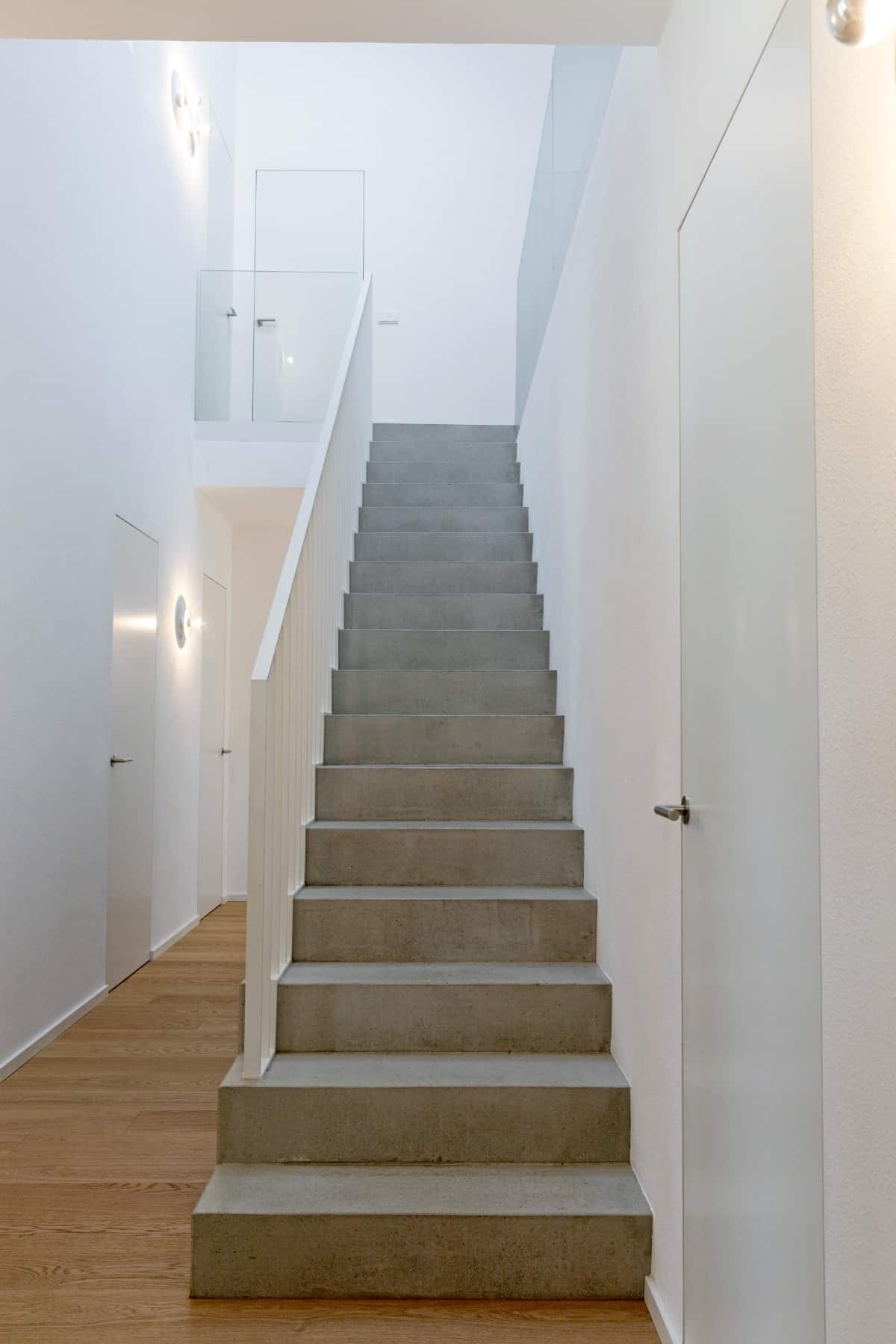 The concrete staircase with white handrails leads to the upstairs bedrooms.