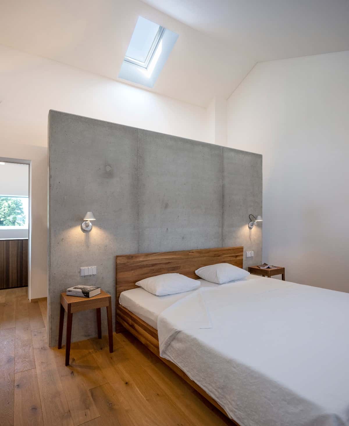 This bedroom features a concrete headboard which adds playful contrast to the wooden furnishing and hardwood flooring.