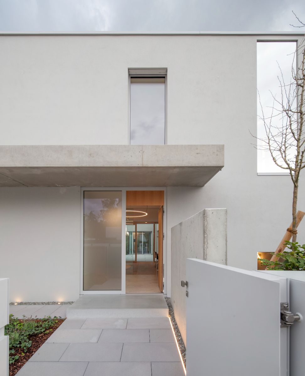 The house's main entry with concrete pavers leading to the main door made of glass with a concrete overhang. The front yard has a garden.