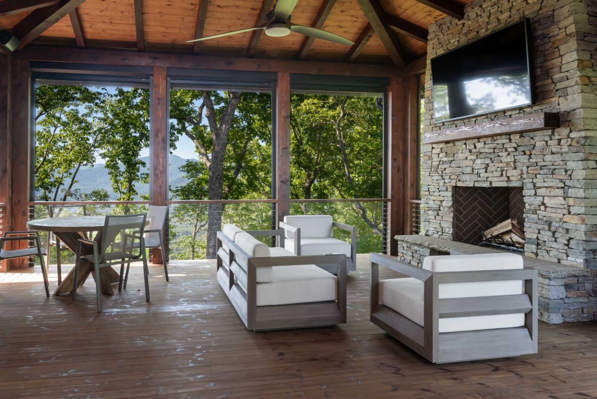 An open layout of the family room with fireplace and breakfast nook boasts stone accent walls, a copper ceiling, and large windows that provide a full view of the surrounding trees.