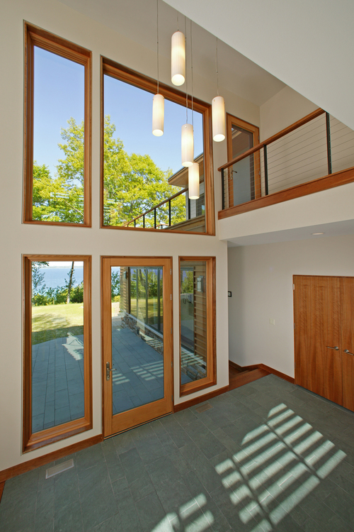 The horizontal batten cedar cladding is cut open and lifted to become a louvered sunscreen for the double height entry space, which glows like a lantern in the evening.