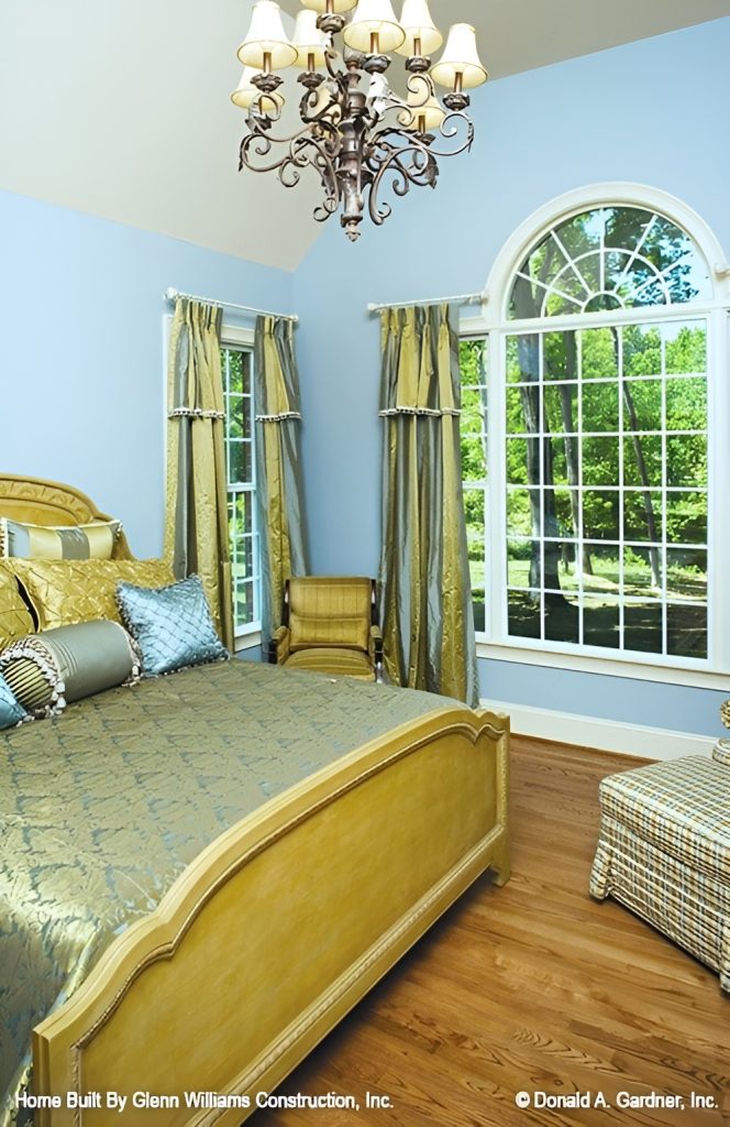 Primary bedroom with a classy bed, light blue walls, and a palatial window dressed in striped draperies.