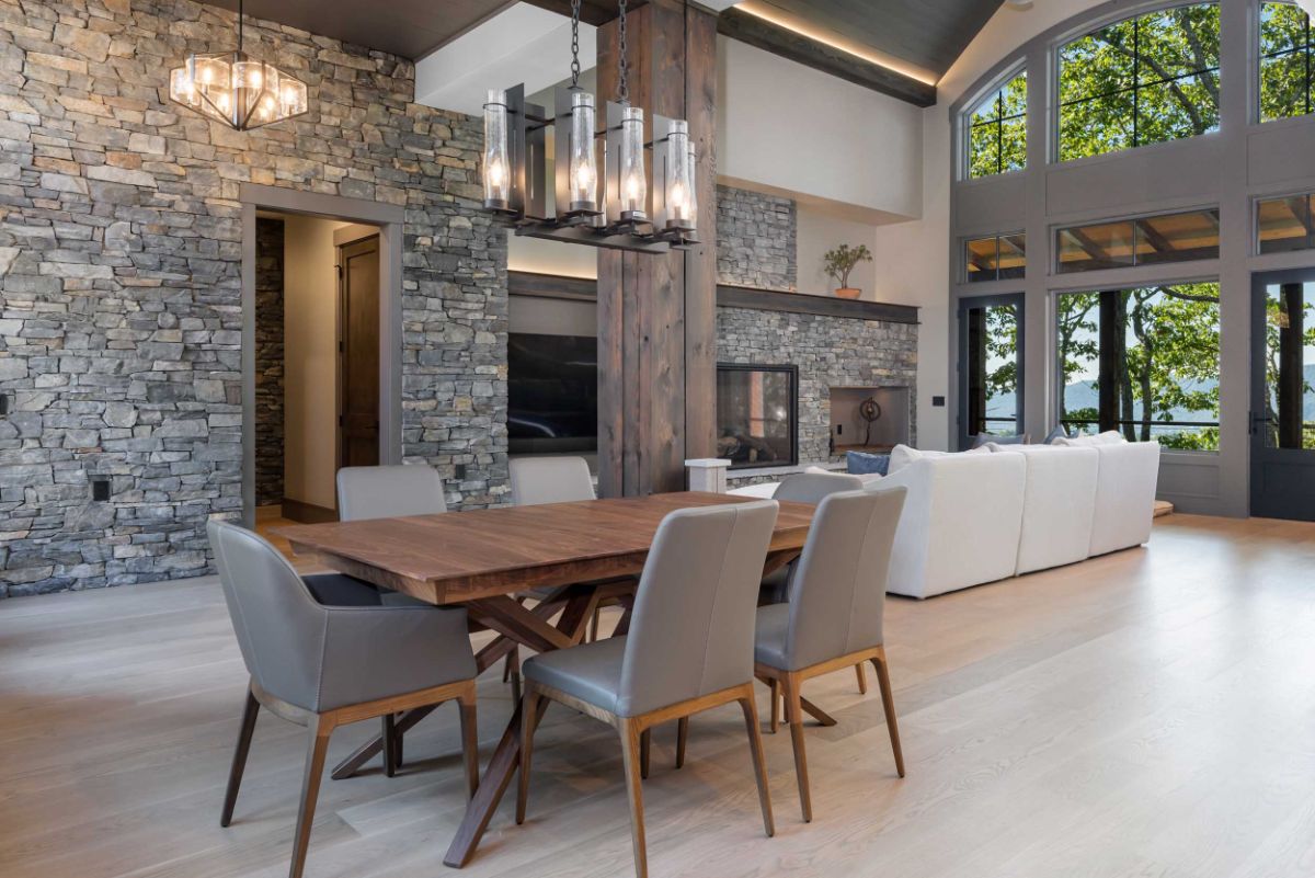 An eye-catching design is created by a double-height formal dining and living area adorned with contemporary lighting, stone accent walls, and expansive windows.