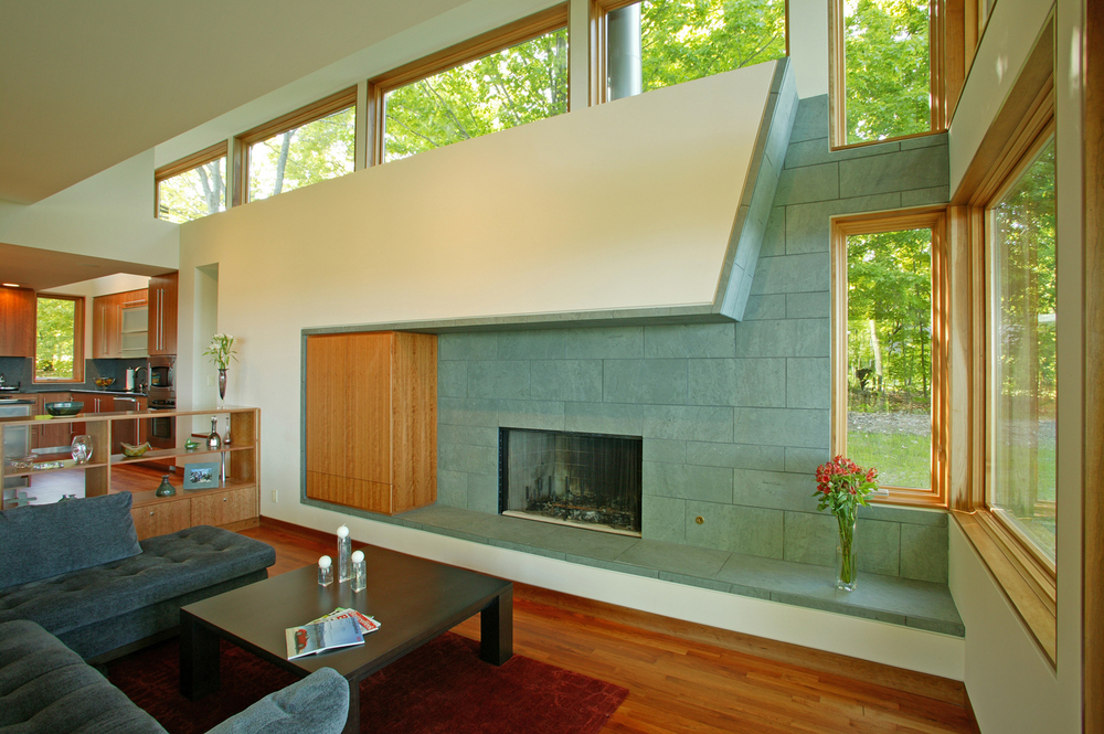 The living area features cherry hardwood floors, a wall-mounted wooden fireplace, and clerestory windows that provide views of the tree canopy above. 